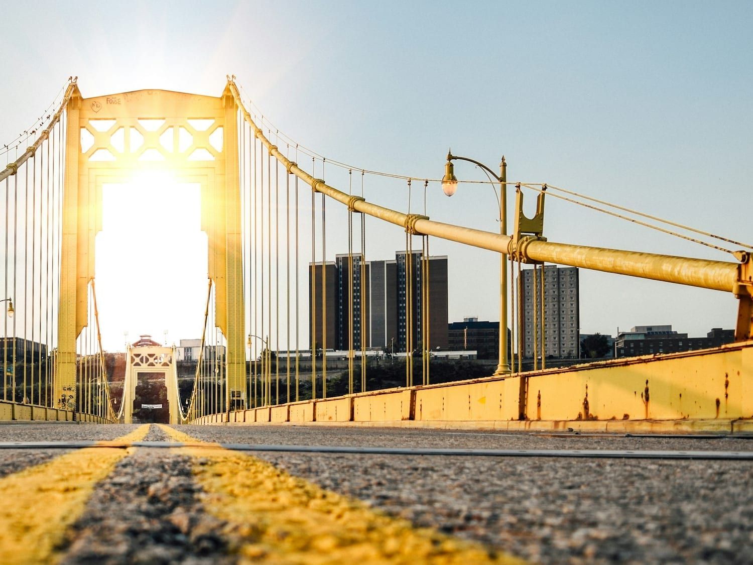Low angle along the deck of a yellow Pittsburgh suspension bridge into the evening sun