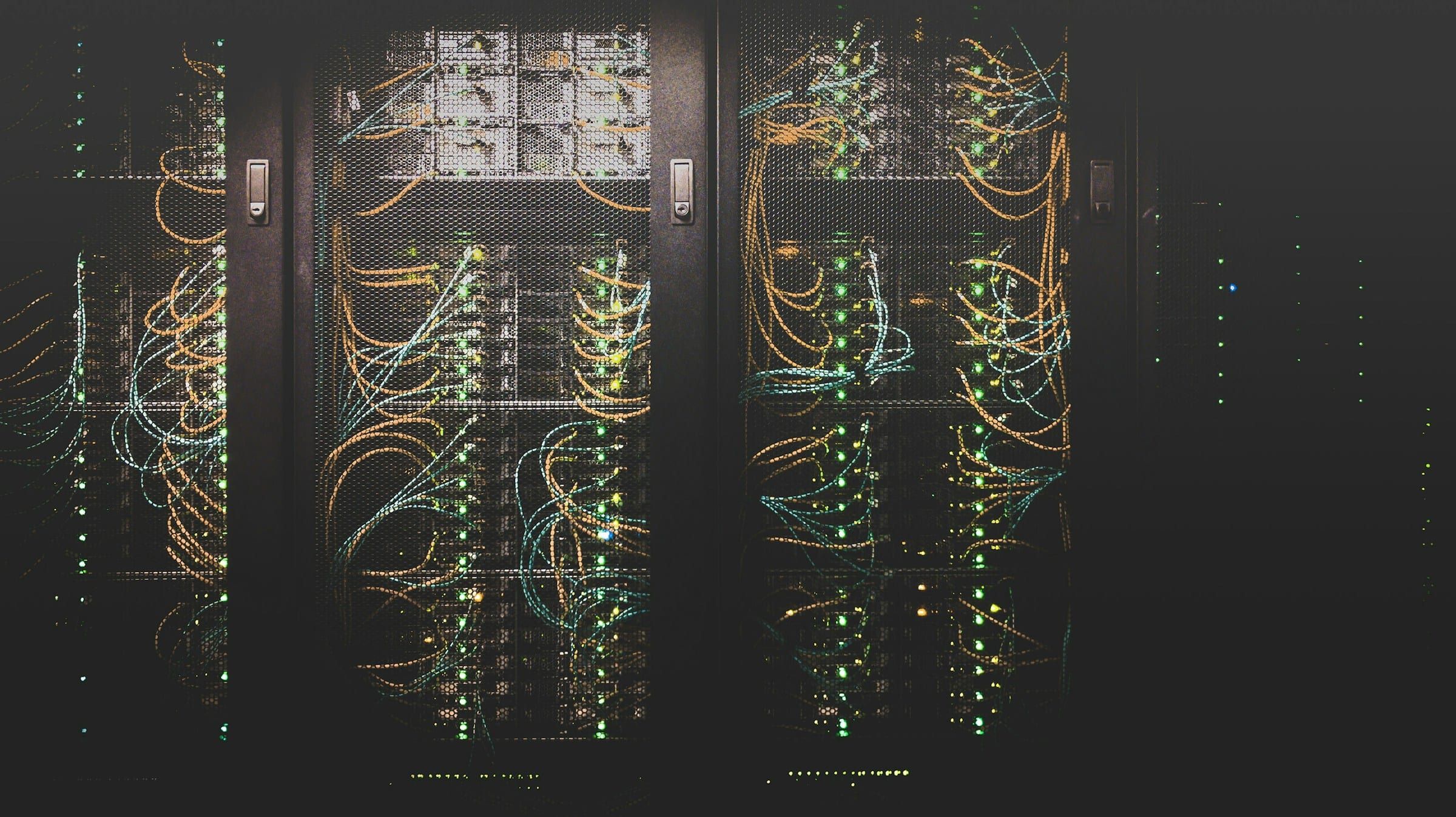 A dim server room aisle with illuminated network cabling running through equipment racks