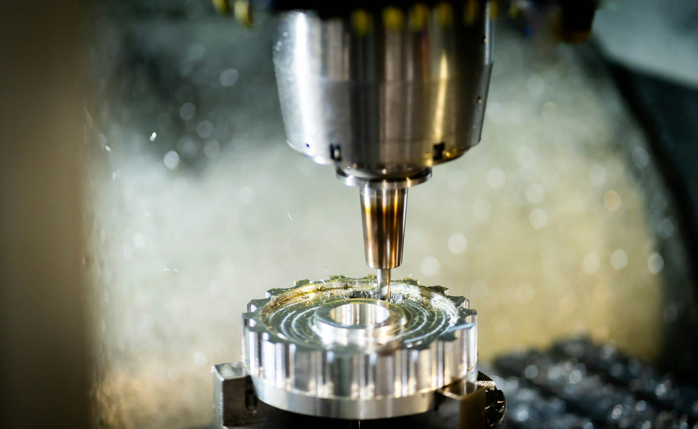 A CNC spindle machining a metal gear while coolant sprays across the cut